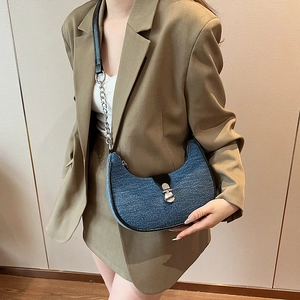 Denim baguette bag with silver chain strap and metal buckle worn as a stylish shoulder bag