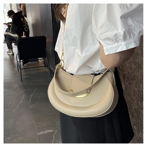 Detail of beige crescent shoulder bag featuring gold hardware and smooth leather texture