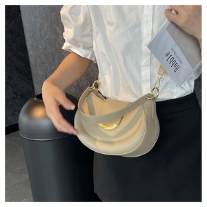 Close-up of beige crescent bag with gold buckle detail worn by a model in casual attire