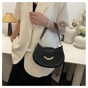 Detail of black crescent shoulder bag with golden U-shaped buckle on beige blazer