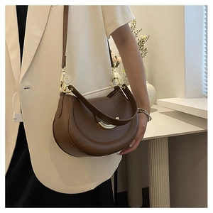 Brown leather crescent bag with golden metal hardware and adjustable shoulder strap worn by model