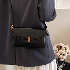 Minimalist black leather crossbody bag with gold buckle on a model with grey blazer