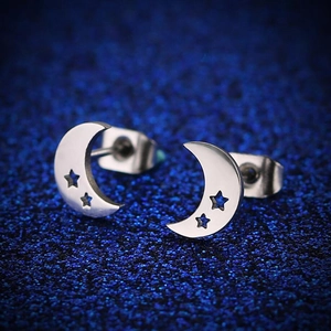 Macro shot of silver crescent moon stud earrings with star cutouts on blue glitter background