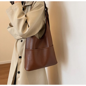 Détail du sac hobo en cuir souple marron foncé avec texture grainée sur l'épaule du mannequin