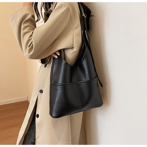 Détail du sac cabas en cuir grainé noir avec poche frontale porté sur un trench-coat beige