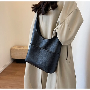 Vue latérale d'un grand sac à bandoulière noir à texture litchi dans un décor minimal