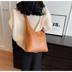 Détail du sac hobo en cuir grainé caramel porté par un mannequin dans un cadre intérieur