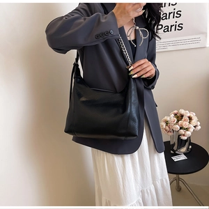 Close-up of minimalist black half-moon shoulder bag with silver chain strap on model