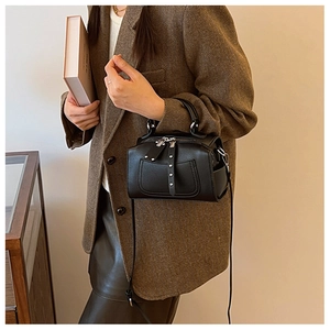 Detail of black Boston bag with silver rivets held by a model in a vintage blazer