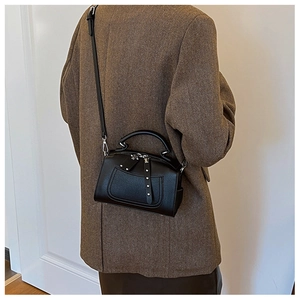 Detail view of black lychee grain crossbody bag with metal rivets on a tailored blazer