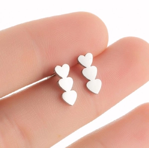 Polished silver stainless steel triple heart stud earrings shown held by hand