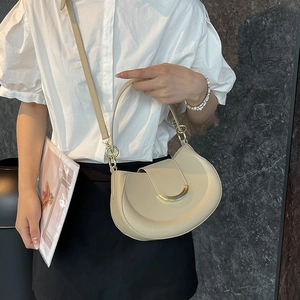 Elegant beige crescent shoulder bag with gold hardware worn by a model in a luxury setting