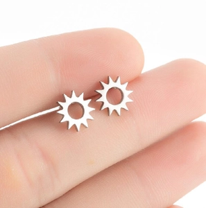 Close-up of silver sunburst stainless steel stud earrings held by hand for size reference