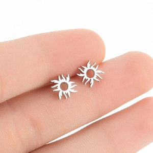 Detail of silver sun-shaped stainless steel stud earrings held by fingers for scale