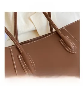 Détail d'un sac cabas en cuir marron avec coutures contrastées sur fond en tissu crème