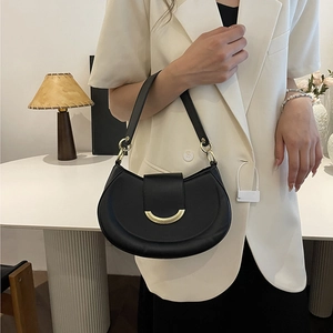 Chic black crescent underarm bag with gold metal clasp shown by a model in a studio