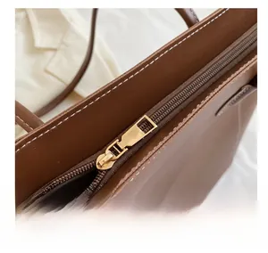 Gros plan sur la fermeture éclair dorée et les coutures blanches du sac cabas marron