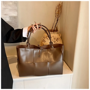 Detail view of deep brown woven leather tote bag with wide textured weave and soft finish