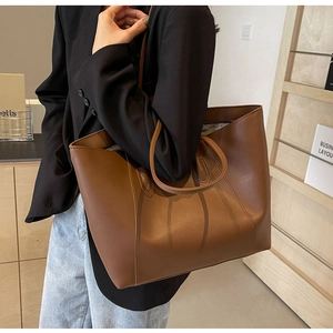 Close-up of a large caramel brown leather tote bag worn by a model in a minimalist room