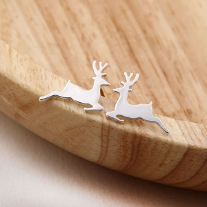 Macro shot of silver reindeer earrings on a natural wood surface for Christmas