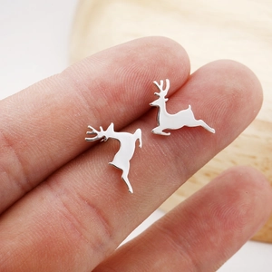 Close-up of small silver reindeer stud earrings held on a finger for size reference