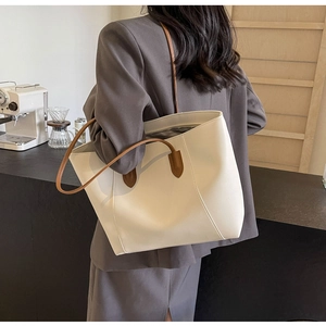Detailed view of cream tote bag with dark brown contrast handles on a model shoulder
