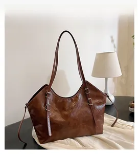 Dettaglio della texture in pelle cerata marrone e fibbie metalliche di una grande borsa tote