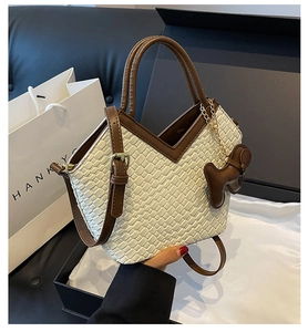 Detail der beige geflochtenen Tragetasche mit braunen Kontrastriemen und Bärenanhänger