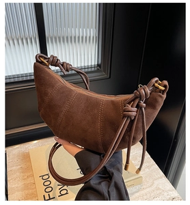 Detail of a brown suede crescent bag featuring a stylish knotted strap and metal zipper