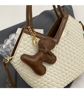 Detail der geflochtenen Eimertasche mit braunem Rand, Plüsch-Anhänger und Schultergurt