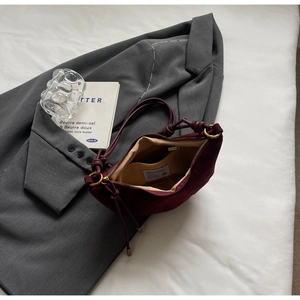 Macro detail of wine red suede crossbody bag featuring knot strap and interior pocket