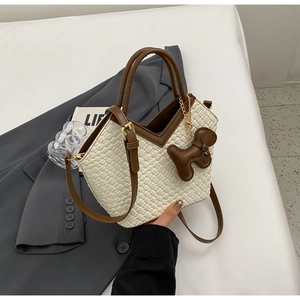 Detail der cremefarbenen Web-Beuteltasche mit braunem Kontrastrand und Hundeanhänger