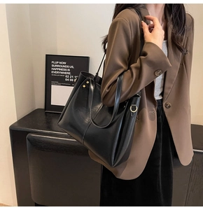 Detail of a large black leather tote bag featuring golden D-ring and slender shoulder strap