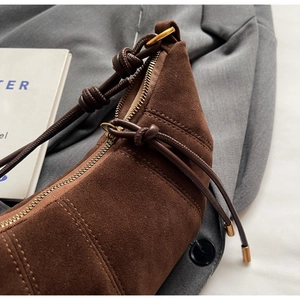 Detail of brown suede crescent bag featuring leather knot strap and gold metal hardware