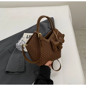 Detail der braunen geflochtenen Eimertasche mit Bärenanhänger und verstellbarem Gurt