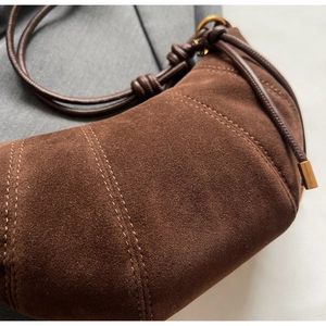 Detail of dark brown suede crescent bag with quilted stitching and knotted leather strap