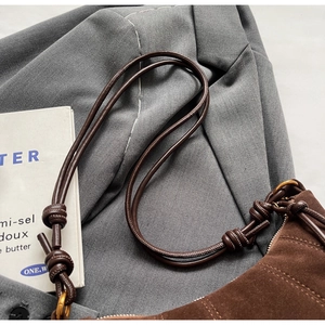 Close-up of brown suede shoulder bag with tubular knotted strap and gold hardware