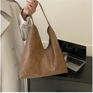 Macro detail of large brown soft leather tote bag showing smooth matte texture and asymmetric shape