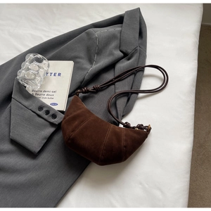 Detail of dark brown suede crescent bag with knot strap on a grey blazer