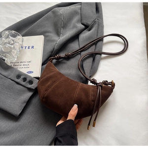 Detail of a dark brown suede croissant bag with vertical stitching on a grey suit