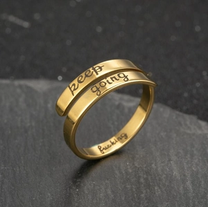 Macro view of gold stainless steel wrap ring with keep going and fucking engraving