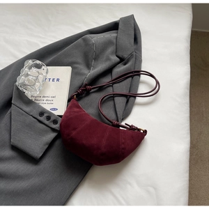 Detail of burgundy suede croissant bag featuring knot strap and textured stitching