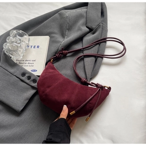 Detailed view of burgundy suede crescent bag with quilted seams and knotted strap