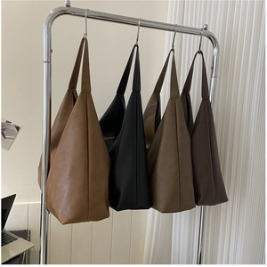 Detail view of large soft leather tote bags in four neutral colors on a metal stand