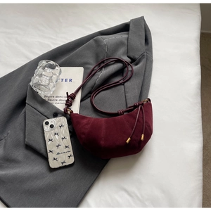 Detail of burgundy suede croissant bag with radial stitching on grey suit