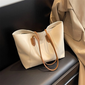 Minimalist cream tote bag with brown straps placed on a leather seat with a trench coat