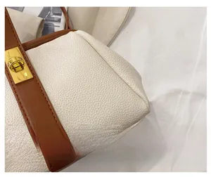 Detail of white lychee leather texture and golden metal twist lock on a shell bag