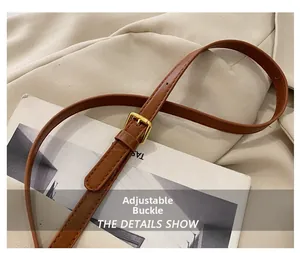 Detail of adjustable brown leather shoulder strap with gold metal buckle and stitching