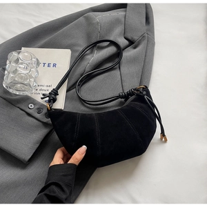 Detailed close-up of a matte black croissant bag with decorative knotted leather straps