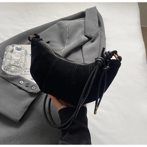 Detailed close-up of a black suede crescent bag with knot strap and gold rings
